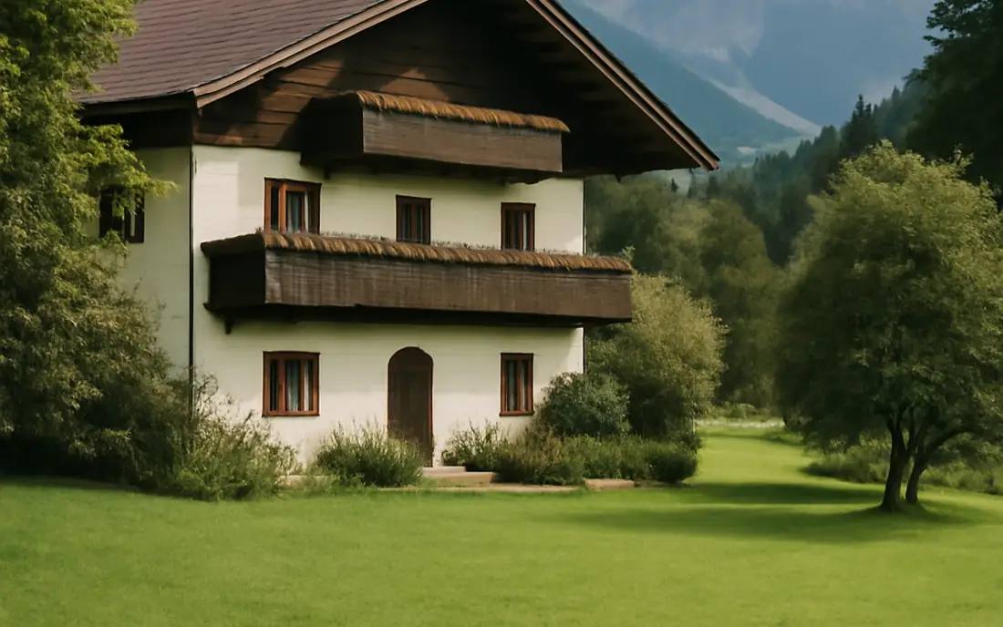 Ein traditionelles österreichisches Haus inmitten von grüner Natur und den Alpen im Hintergrund.